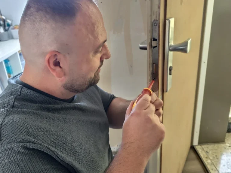 Mann arbeitet mit Werkzeug an einer Tür, um einen Schlossmechanismus zu reparieren.