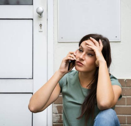 Frau mit Telefon, sieht besorgt und gestresst aus, sitzt an der Wand.